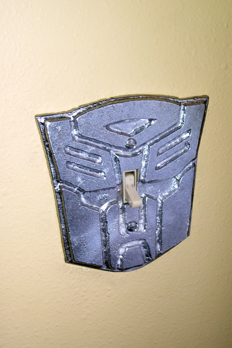 Autobot symbol in quarter-inch sandcast plate aluminum with raised details and appropriate piercings installed over a lightswitch.