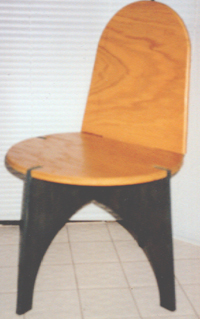 The chair back is secured to the axial leg-piece, through the seat, by a wide tab on its bottom edge. The back secures the seat in place, and is in turn held fast by gravity and friction.