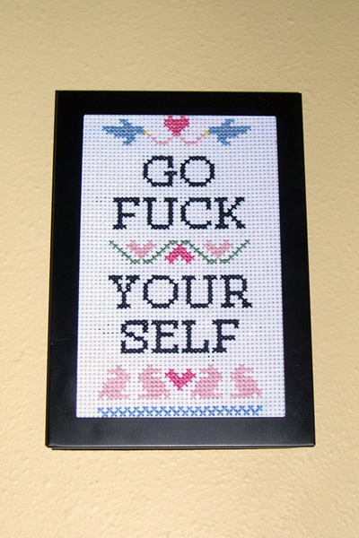 Small cross-stitch sampler in traditional style with decidedly nontraditional text: GO FUCK YOUR SELF.