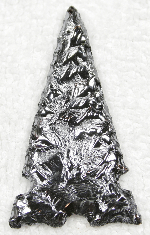 A knapped arrowhead in the style of Native American stone artifacts, in a thoroughly modern, shiny-metal-grey glass.