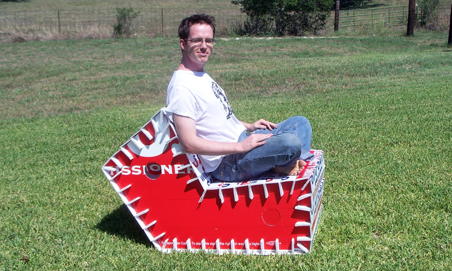 Myself seated in street spam lounger prototype, showing profile against grassy hill.