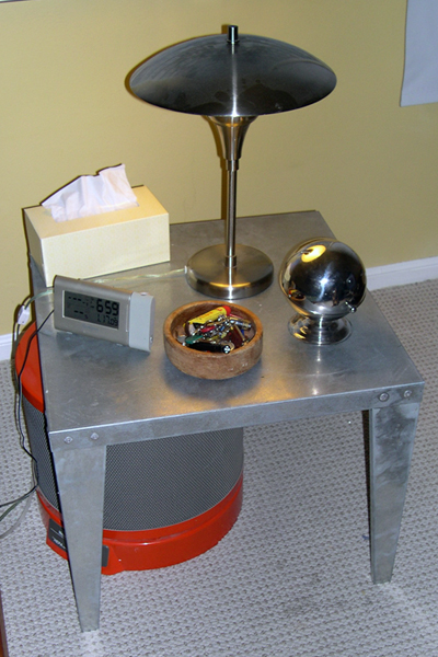A galvanized sheet metal water heater stand serving as bedside table, with matching stainless steel lamp.