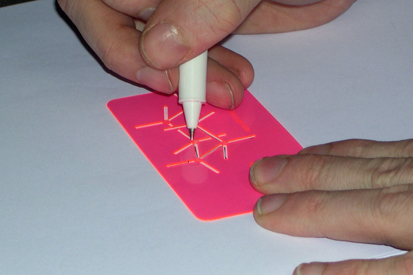 Hands and a pen trace the outline of the chair through the business card, demonstrating its function as a drawing template.